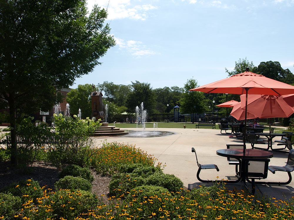 view of splash pad in distance, picnic tables with red umbrellas at right